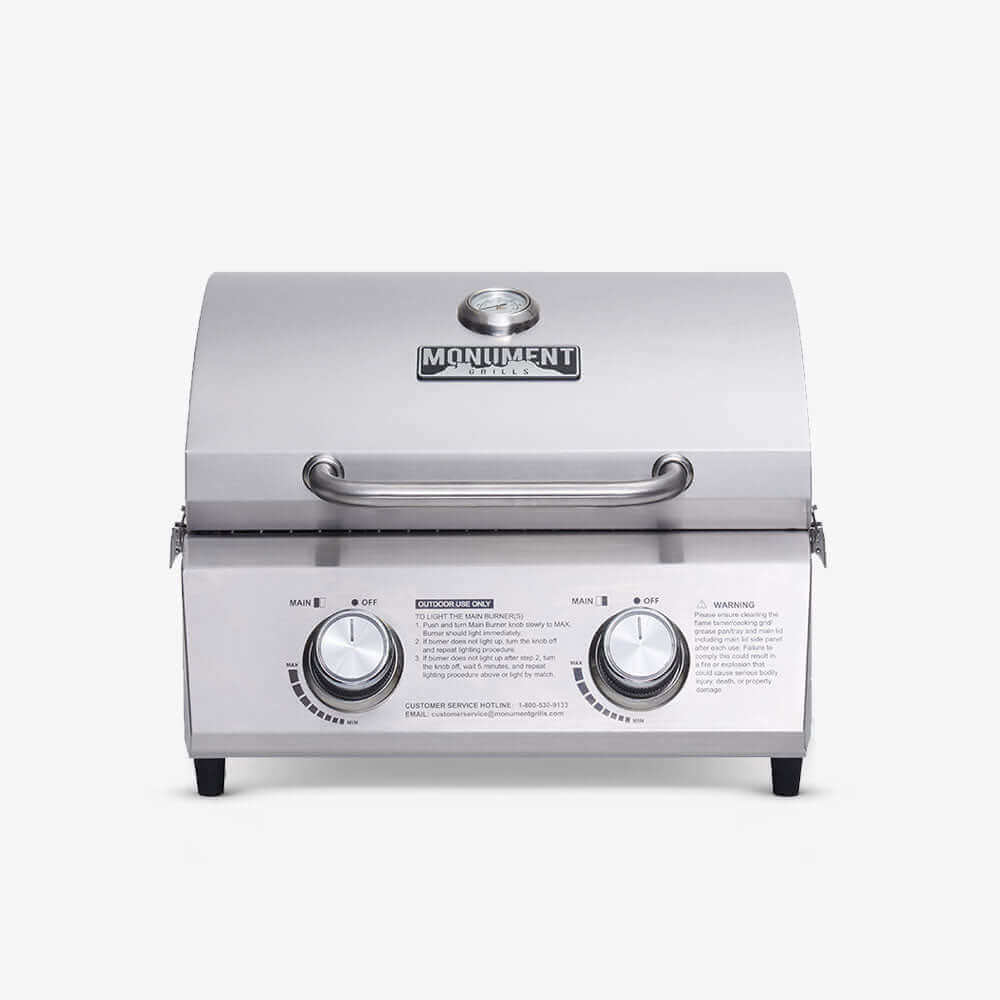 Stainless steel portable tabletop propane gas grill with two burners at an outdoor tailgate