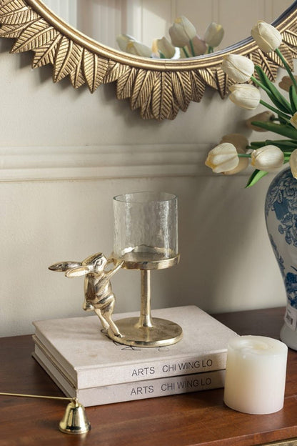 Gold rabbit pillar candle holder with clear glass hurricane shade on an accent table