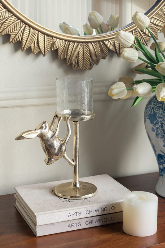 Tall gold rabbit candle holder with glass hurricane shade on a dining room mantel