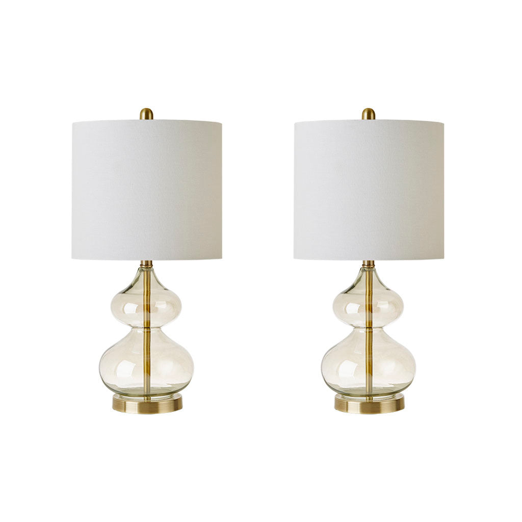Pair of curved glass table lamps with gold bases and white drum shades on matching nightstands