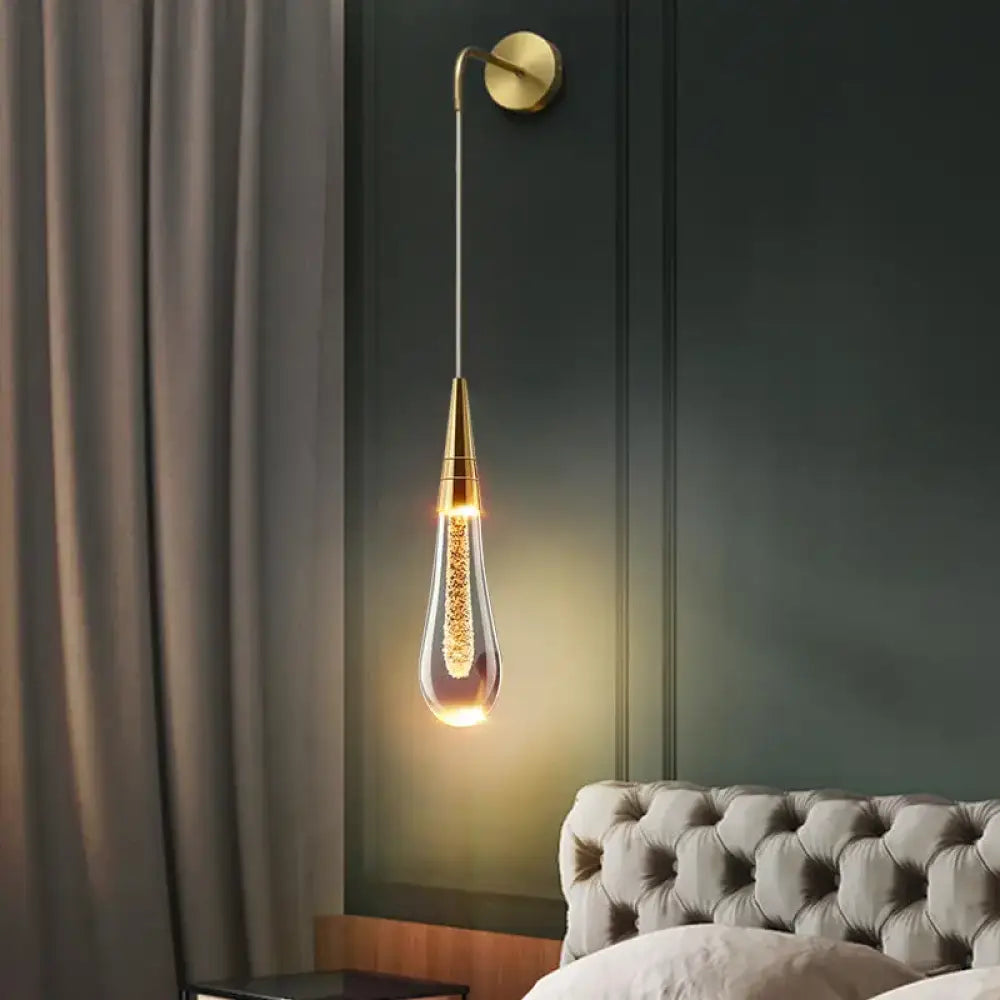 Gold post-modern glass raindrop LED wall sconce glowing beside a bed in a bedroom