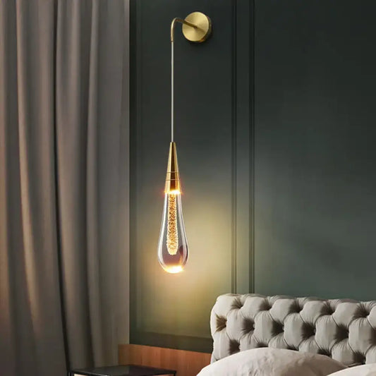Gold post-modern glass raindrop LED wall sconce glowing beside a bed in a bedroom