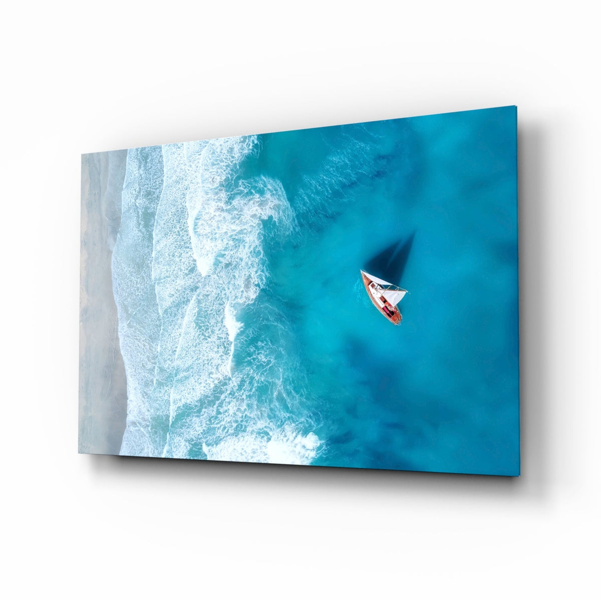 Aerial sailboat glass wall art with turquoise water and sandy shoreline hung in a coastal living room